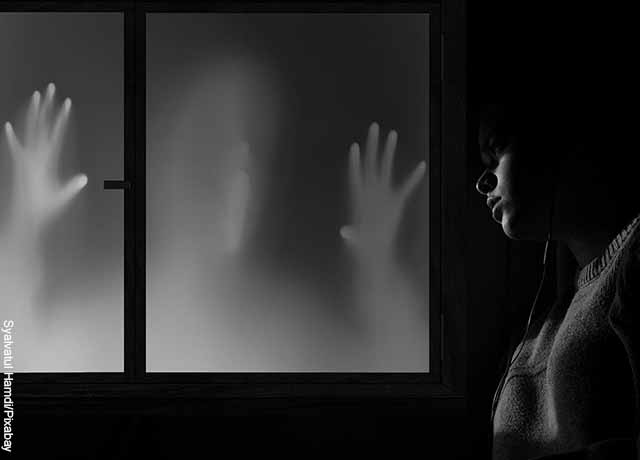 Foto de una mujer frente a la ventana en la que hay unas manos