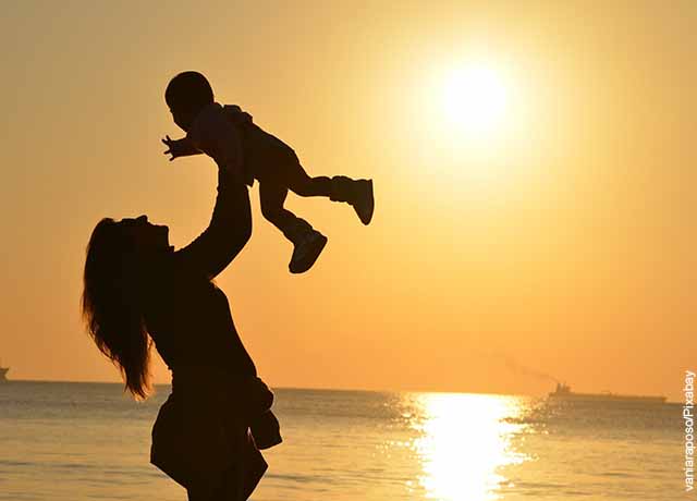 Foto de una mujer alzando a su bebé en la playa que muestra el significado de karma
