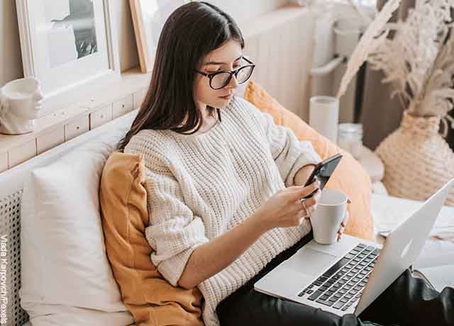 Foto de una mujer mirando la pantalla de su celular con un té en la mano