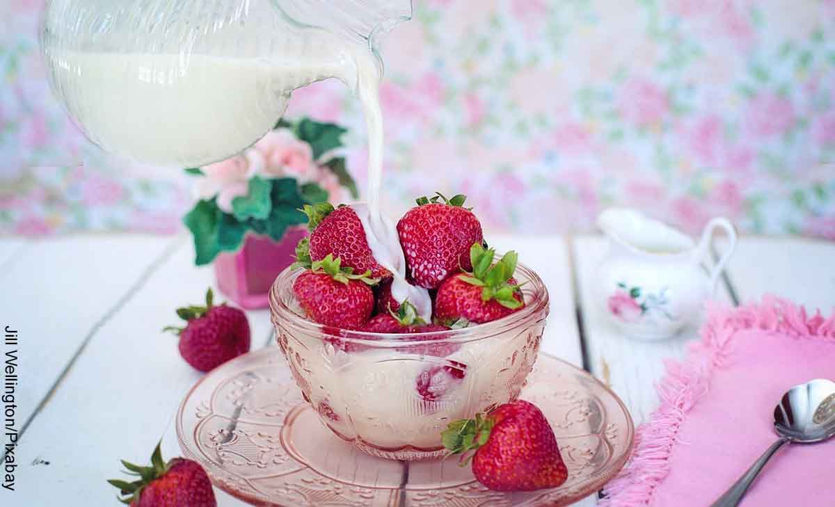 Foto de leche cayendo sobre fresas en un recipiente que muestra los postres con recetas fáciles