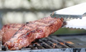 Foto de una persona asando carne en parrilla que revela las recetas de almuerzos caseros colombianos fáciles