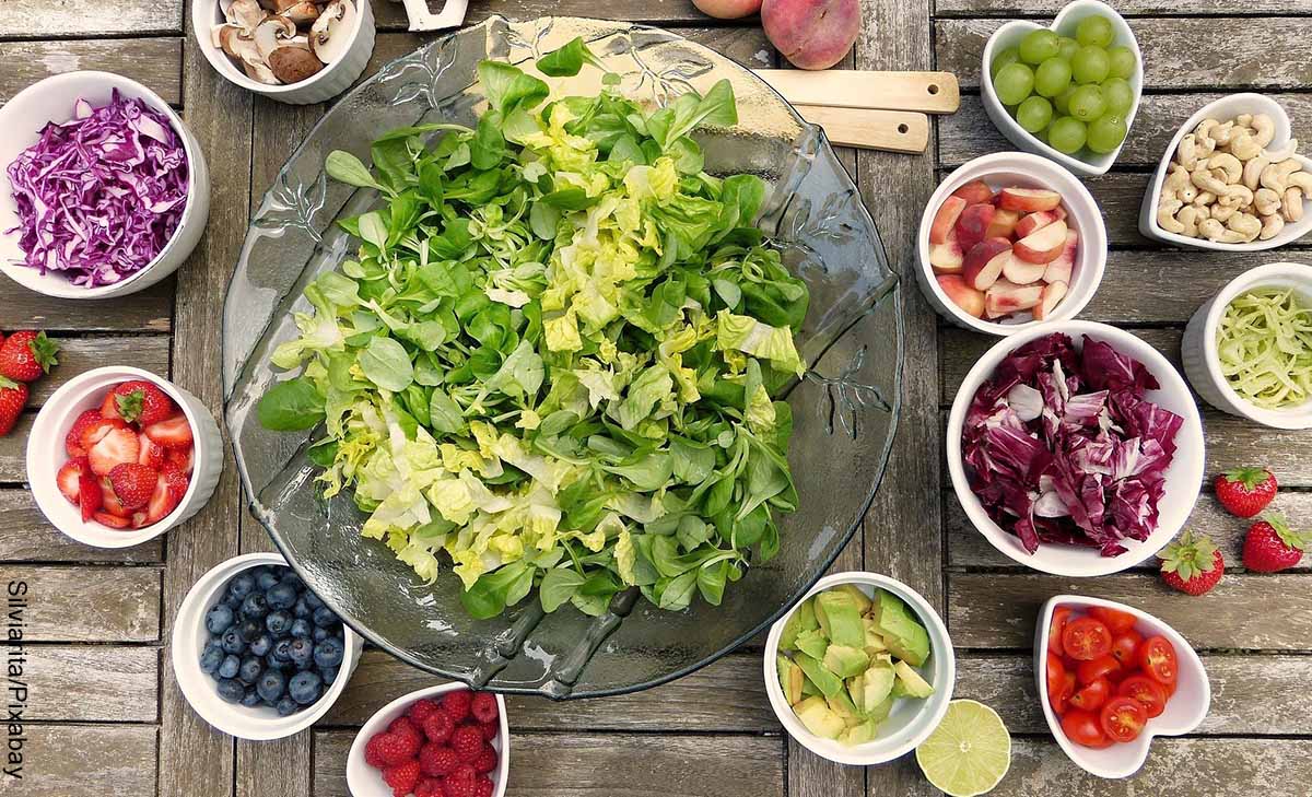 Foto de lechuga en un bol y verduras y frutas sobre la mesa que muestran las recetas de ensaladas
