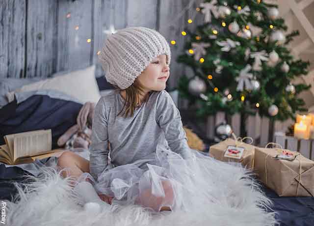 Foto de una niña al lado de un árbol que revela el significado del árbol de Navidad