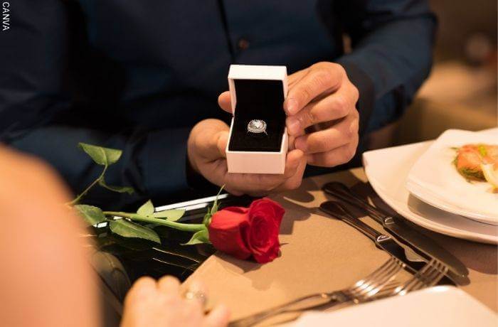 Foto de las manos de un hombre sosteniendo un anillo en su caja pidiendo matrimonio en una mesa de restaurante