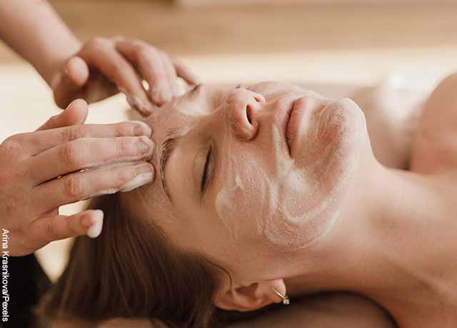 Foto de una mujer a la que le aplican crema en el rostro que muestra un masaje facial