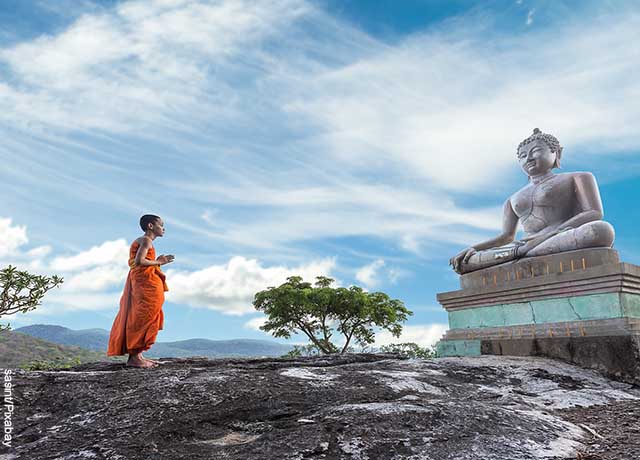 Foto de un niño budista recitando los mantras poderosos frente a una estatua grande