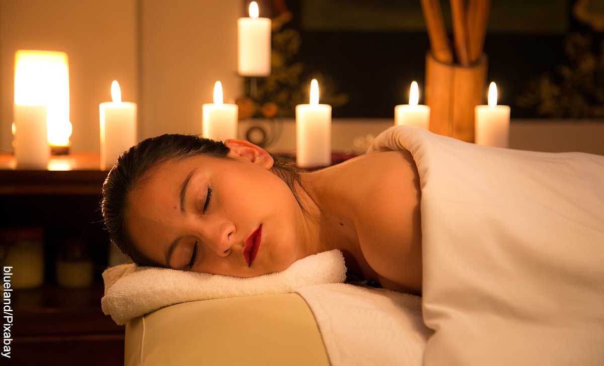 Foto de una joven acostada sobre una cama con velas que revela el masaje nuru