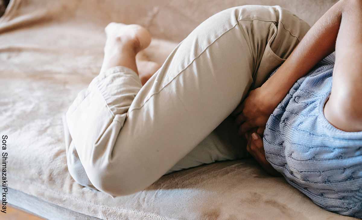 Foto de una mujer acosyada en su cama con dolor de estómago que revela los masajes para el colon
