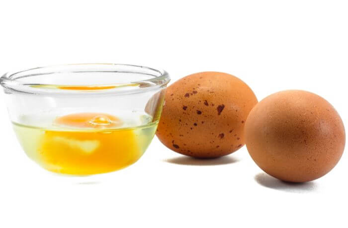 Foto de huevos junto al contenido de uno en un recipiente transparente