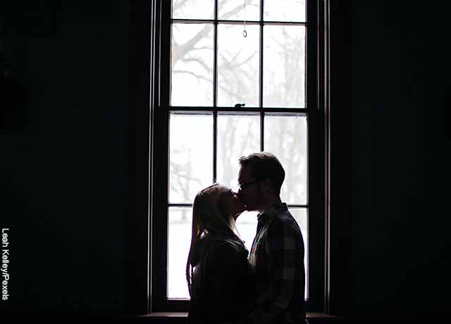 Foto de una pareja joven dándose un beso frente a la ventana