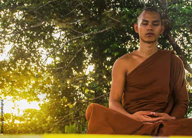 Foto de budista con los ojos cerrados meditando bajo un árbol