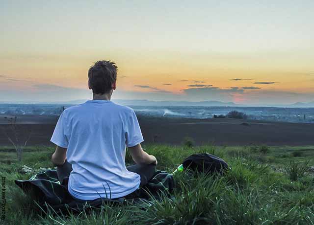 Foto de un joven haciendo meditación en un campo abierto