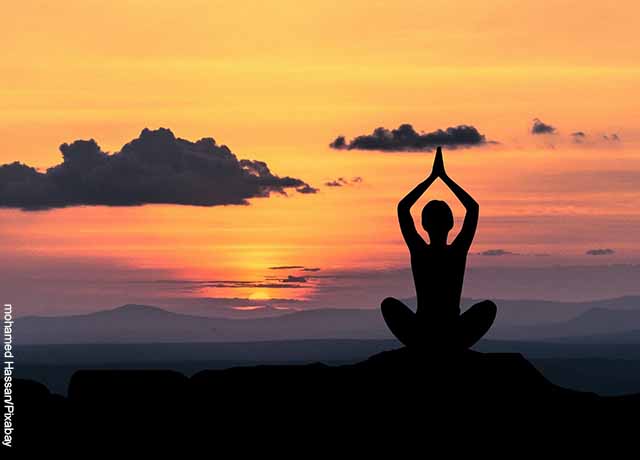 Foto de una mujer haciendo yoga al atardecer que ilustra los mantras positivos