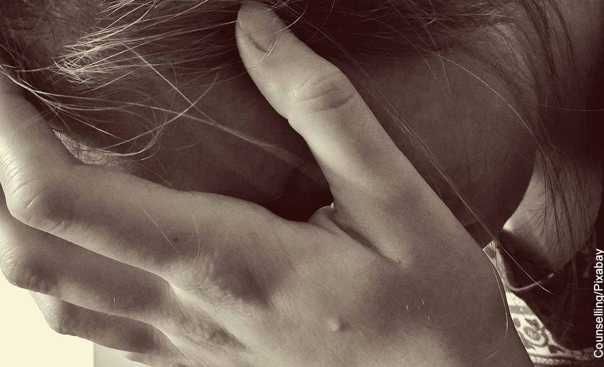 Foto de una mujer llorando tocándose la cabeza que revela los signos de alarma dolor abdominal