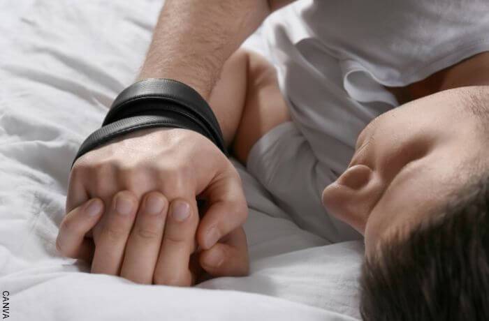 Foto de un hombre en la cama con las manos atadas
