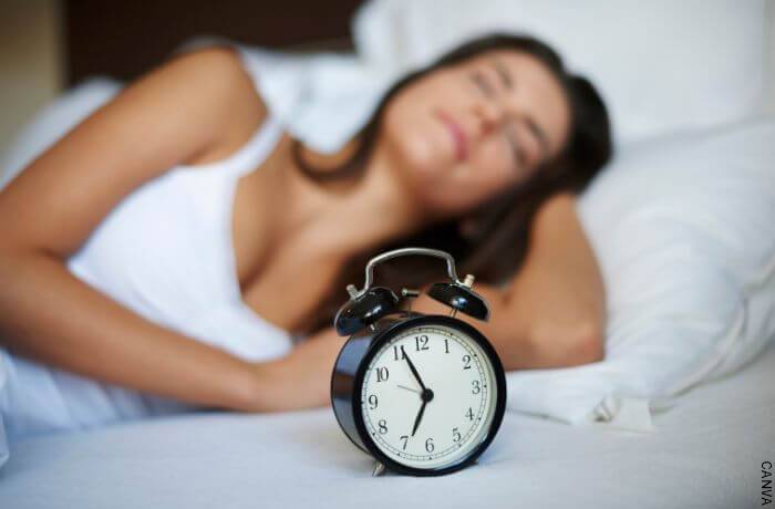 Foto de una mujer en la cama y en primer plano un despertador