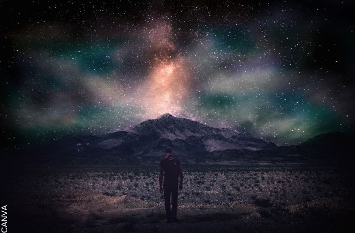 Foto de un hombre caminando hacia una montaña iluminada por las estrellas