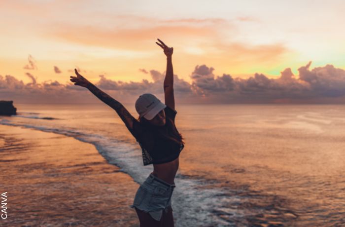 Foto de una mujer con los brazos levantados frente a una playa