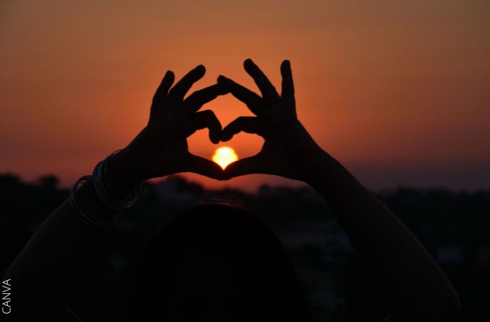 Foto de una mujer haciendo una forma de corazón con sus manos y el sol de fondo