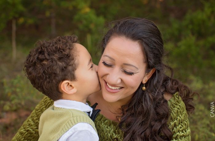Foto de una mamá sonriendo mientras su hijo le da un beso en la mejilla