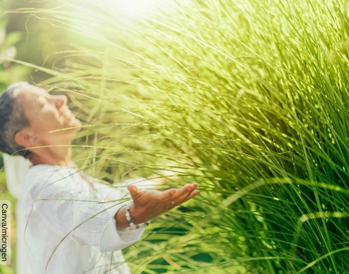 Foto de una mujer con los ojos cerrados y los brazos abiertos frente a un campo de pasto
