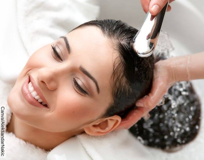 Foto de una mujer sonriendo mientras enjuagan su cabello con agua tibia