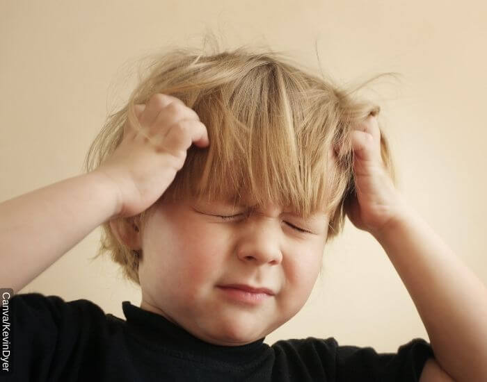 Foto de un niño rubio con los ojos cerrados con picazón en la cabeza a causa de piojos