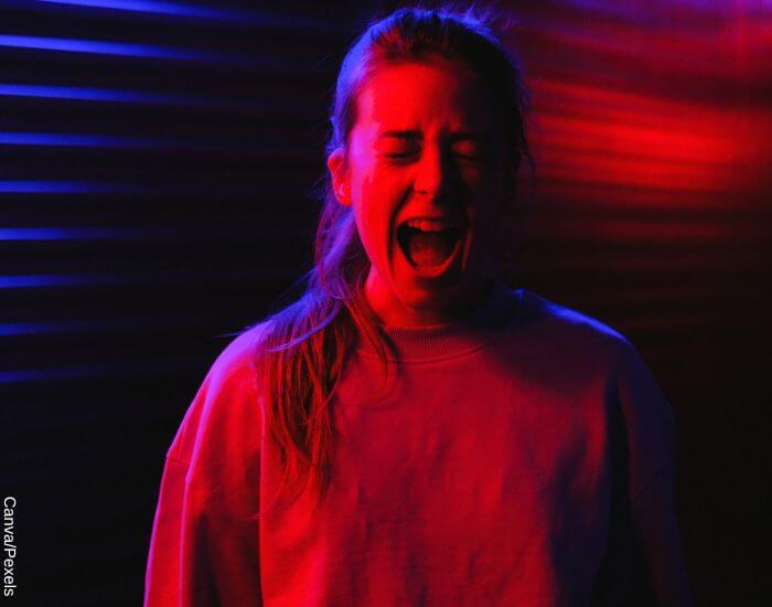 Foto de una mujer gritando con los ojos cerrados en un cuarto con luz roja y azul