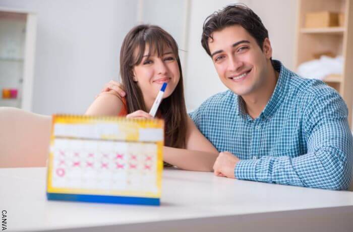 Foto de una pareja detrás de un calendario con una prueba de embarazo