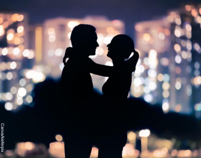 Foto de una pareja abrazada sonriendo ante el reflejo de las luces nocturas de la ciudad