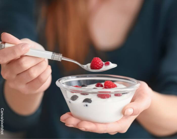 Foto de una mujer dando una cucharada a su taza de yogurt con fruta