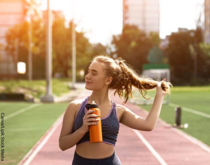 Foto de una mujer haciendo ejercicio al aire libre mientras toma agua de un botilo