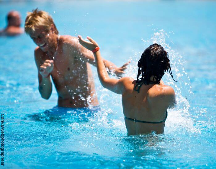Foto de una pareja jugando a salpicarse con agua dentro de una piscina