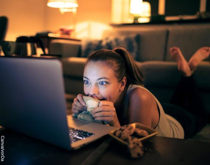 Foto de una mujer viendo una película en la sala de su casa con si cabeza muy cerca de la pantalla de su computador