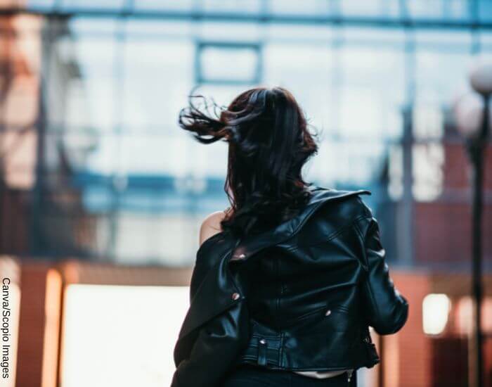 Foto de una mujer de espaldas caminando frente al viendo usando una chaqueta de cuero negra