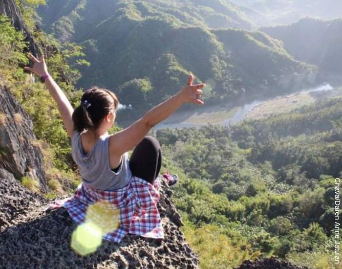 Foto de una mujer signo Acuario subida en una roca en la cima de una montaña mirando hacia la naturaleza con los brazos abiertos