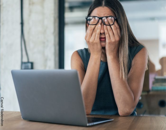 Foto de una mujer ejecutiva sentada frente a un computador rascando sus ojos por el cansancio del día