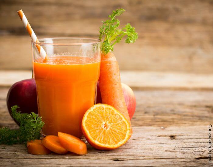 Foto de un vaso de jugo de naranja, zanahoria y remolacha con los ingredientes detrás