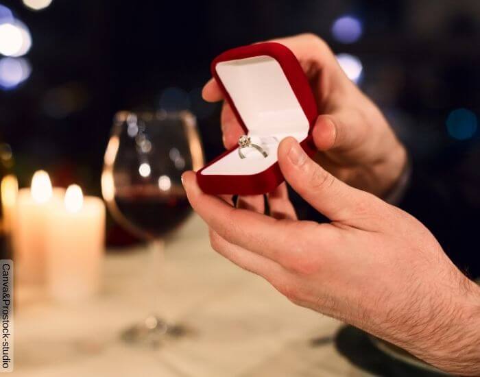 Foto de un anillo de matrimonio en un cofre siendo entregado por un hombre durante una cena romántica