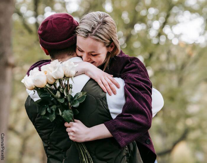 Foto de una pareja abrazada en el bosque, la mujer tiene un ramo de rosas en su mano y está sonriendo