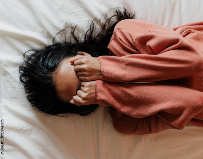 Foto de una mujer boca arria sobre la cama con sus manos cubriendo su cara