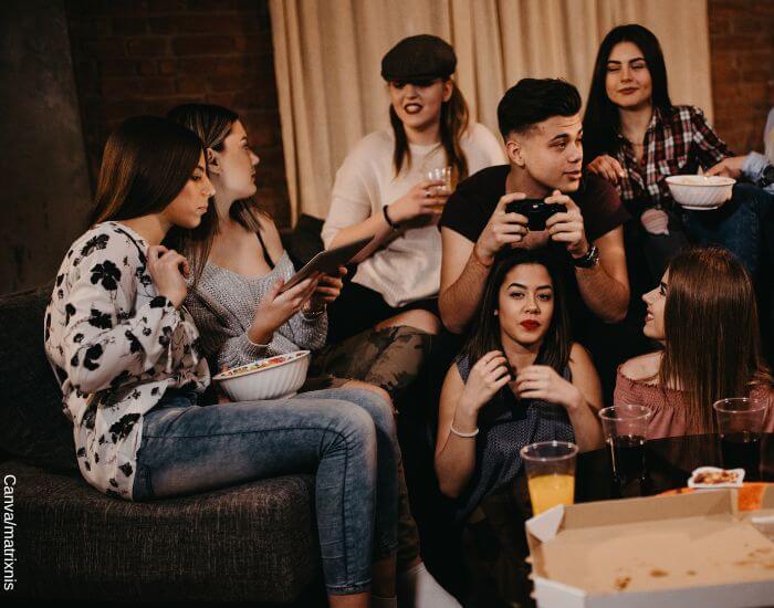 Foto de un grupo de adolescentes entados en un sofá en una fiesta en casa con refrescos y pizza