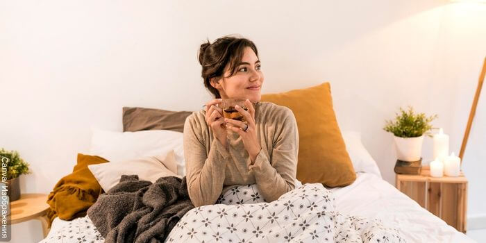 Foto de una mujer sonriente en la cama lista para irse a dormir con una tasa de té de poleo en sus manos