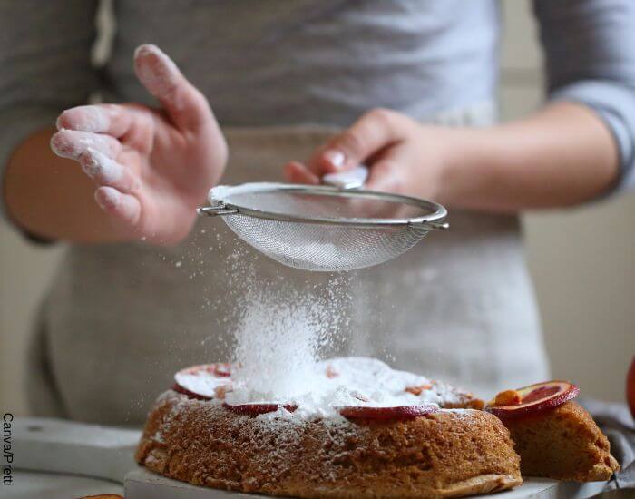 Foto de una persona rociando azúcar en polvo sobre una torta con un colador