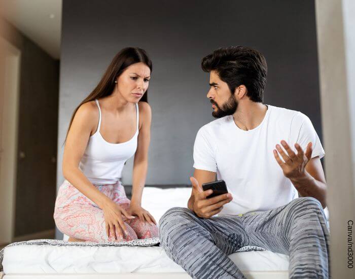 Foto de una pareja en pijama peleando por algo que hay en el teléfono del hombre
