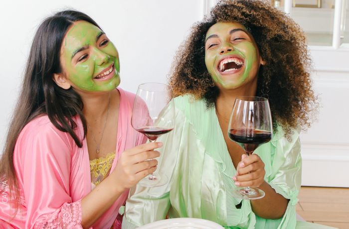 Foto de amigas riéndo con mascarilla verde en la cara y tomando vino