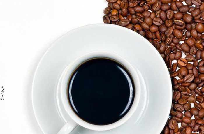 Foto de una taza de café oscuro con granos de café debajo