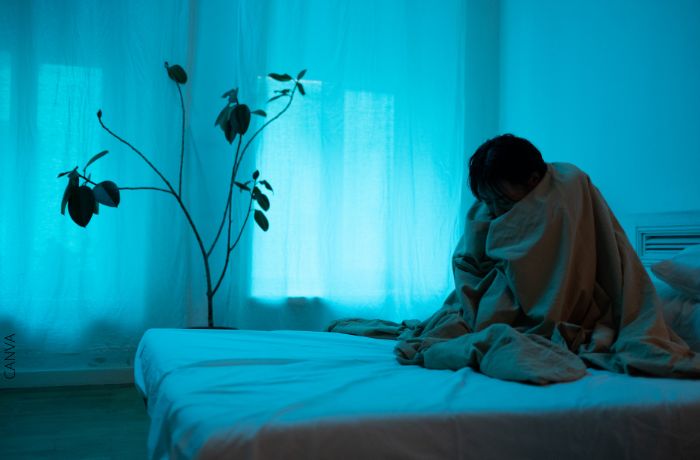 Foto de una mujer sentada en la cama y tapada con una cobija