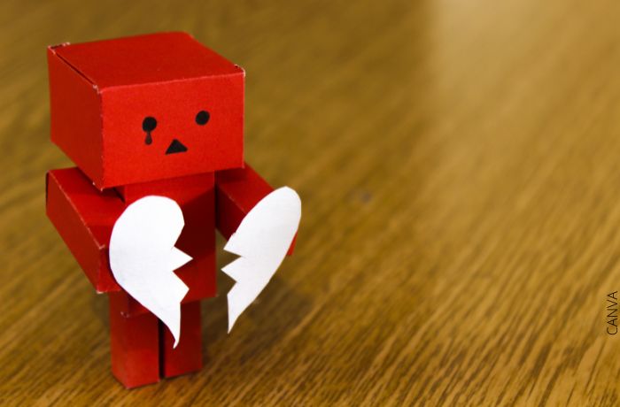 Foto de un muñeco de cartón rojo con un corazón blanco roto