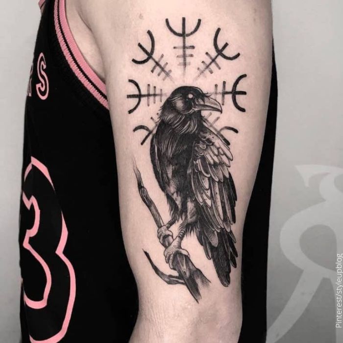 Foto d eun tatuaje de un cuervo con símbolos nórdicos de fondo
